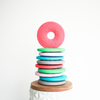 Stack of donut shaped teether toys multi colored with dark pink donut on top standing up