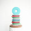 Stack of donut shaped teether toys multi colored with light blue donut on top standing up