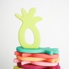 Flat stack of pineapple silicone teethers, one chartreuse Teether upright on top. White background. 