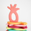 Flat stack of pineapple silicone teethers, one coral Teether upright on top. White background. 