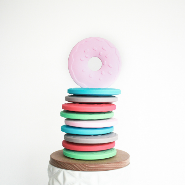 Stack of donut shaped teether toys multi colored with light pink donut on top standing up