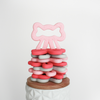Stack of bow shaped teething toys with one pink colored bow sitting upright on top of stack