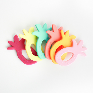 Six pineapple teethers, different colors. White background. 