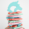 Flat stack of unicorn silicone teethers with cyan blue unicorn upright on top