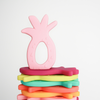 Flat stack of pineapple silicone teethers, one taffy Teether upright on top. White background. 