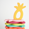 Flat stack of pineapple silicone teethers, one marigold Teether upright on top. White background. 