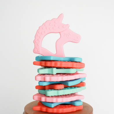 Flat stack of unicorn silicone teethers with taffy pink unicorn upright on top
