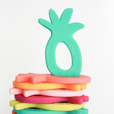 Flat stack of pineapple silicone teethers, one tropical Teether upright on top. White background. 
