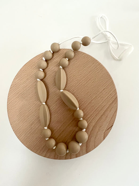 Taupe silicone beaded teething necklace laying on a flat wooden circle