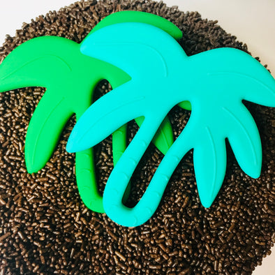 Two palm tree teething toys on an island of brown sprinkles. 