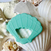 Tropical seashell Teether, shell and sand background. 